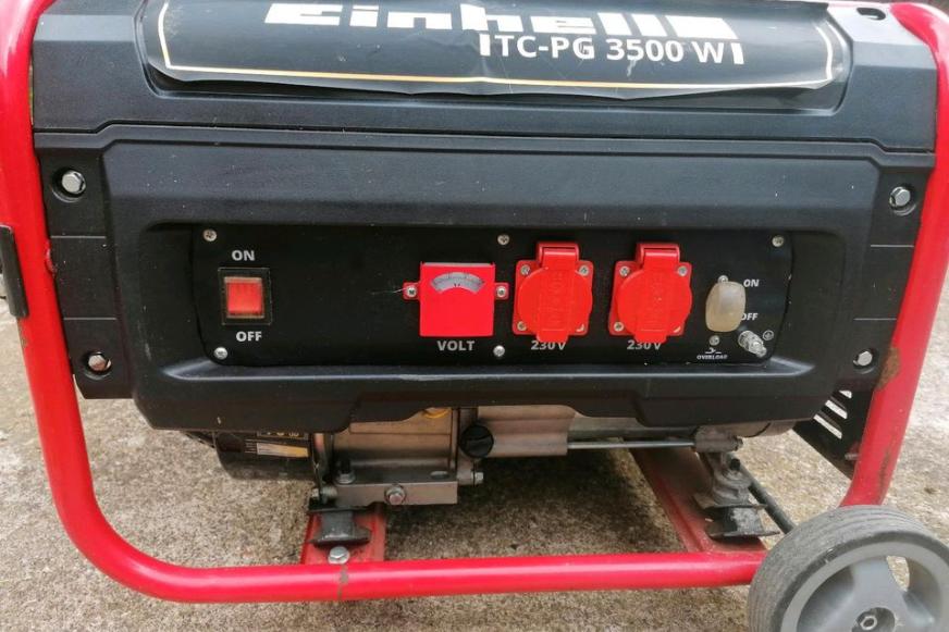 Der Einhell TC-PG 35/E5 Notstromaggregat steht auf der Wiese und wird von der Seite samt den 2 Schuko Steckdosen und dem Voltmeter gezeigt.